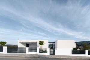 Jednopodlažní moderní dům s plochou střechou a jednoduchou bílou fasádou při pohledu z ulice.