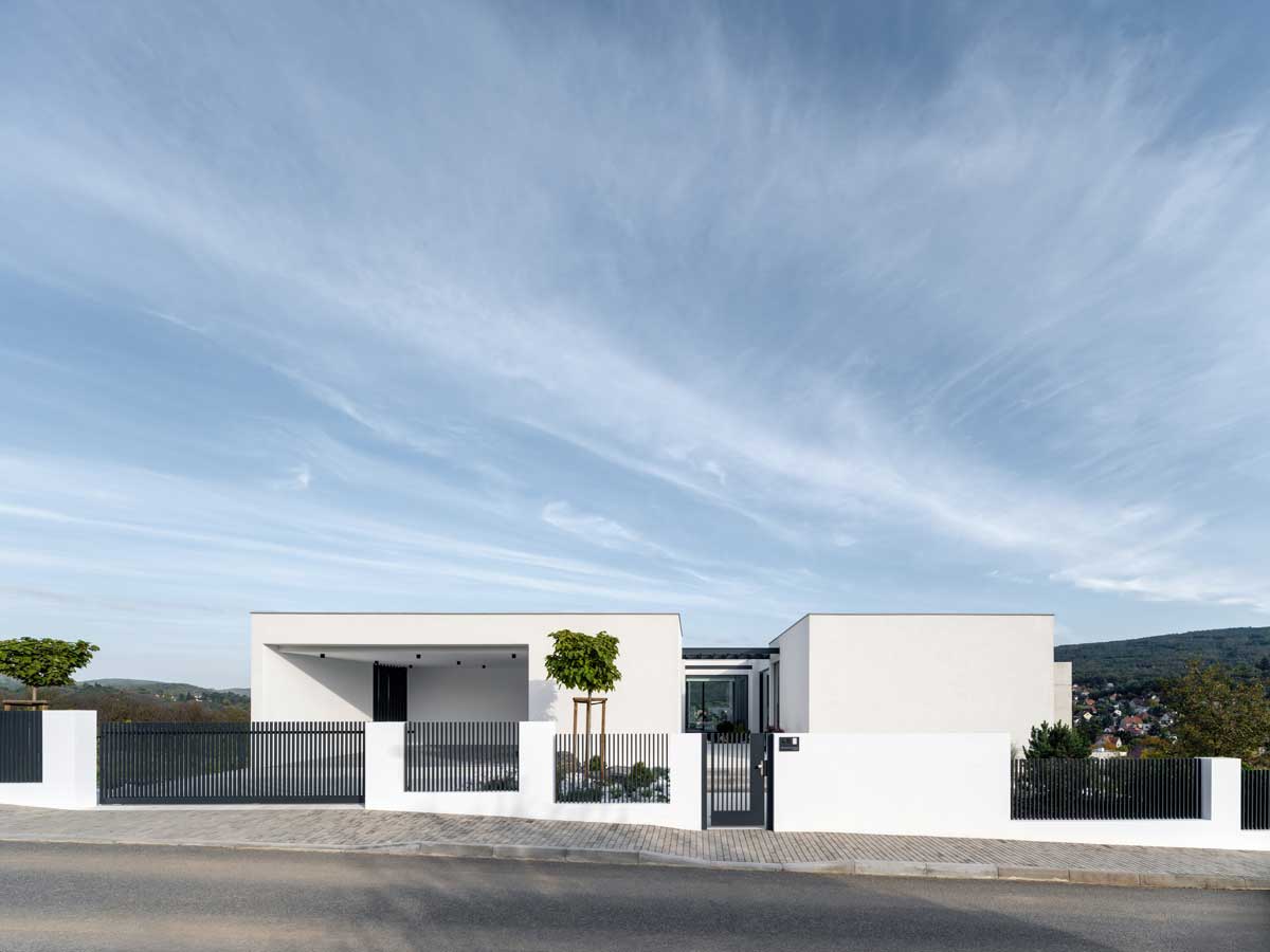 Jednopodlažní moderní dům s plochou střechou a jednoduchou bílou fasádou při pohledu z ulice.