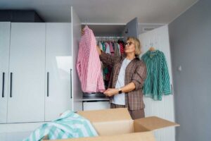 Žena třídí oblečení ve skříni a vybírá kusy vhodné k darování nebo prodeji během domácího detoxu.