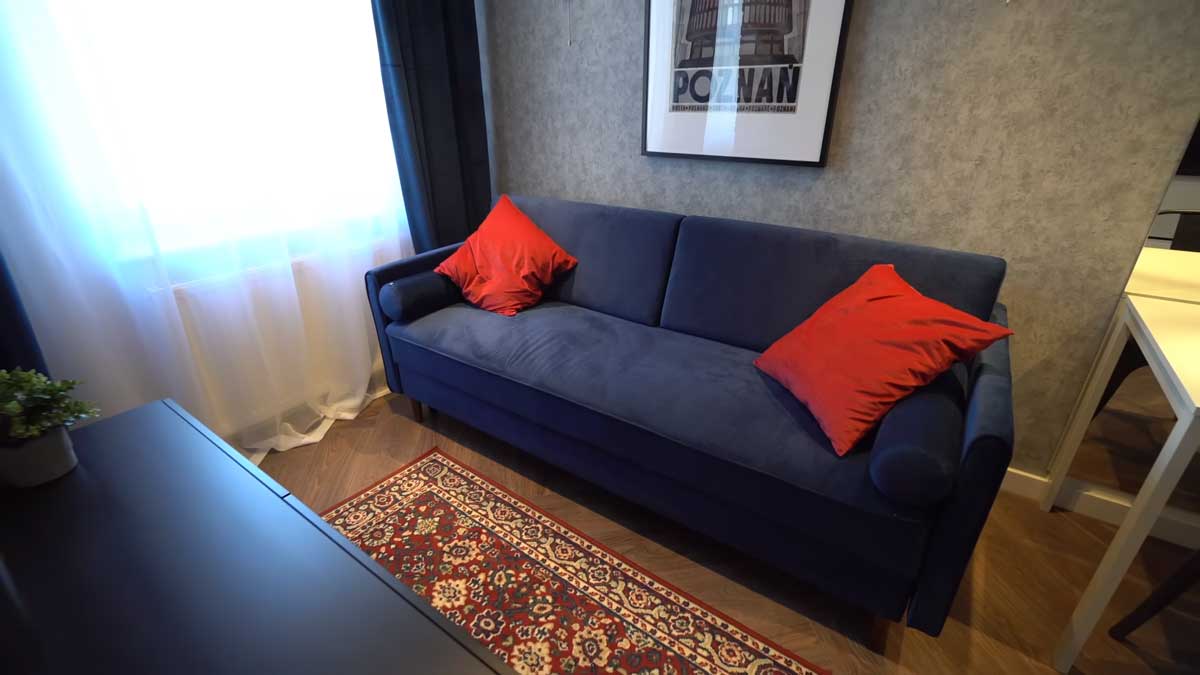 Obývací kout s modrou pohovkou, cihlovou stěnou a textiliemi, které zjemňují industriální styl malého bytu