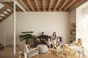 Obývací pokoj s přiznanými dřevěnými trámy, minimalistickou pohovkou a rodinou při společném posezení.