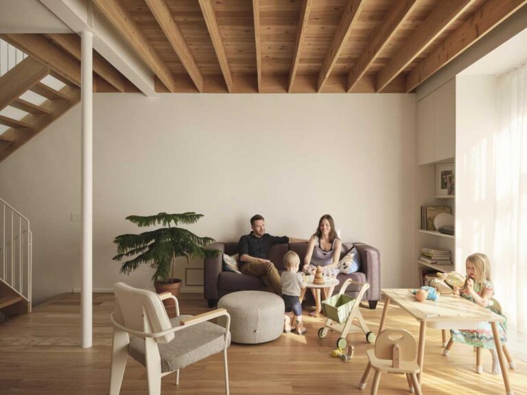 Obývací pokoj s přiznanými dřevěnými trámy, minimalistickou pohovkou a rodinou při společném posezení.