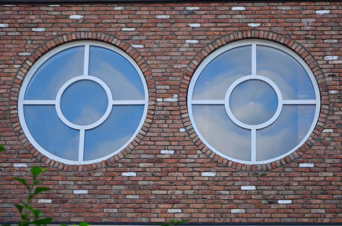 Kruhová okna zasazená do cihlové fasády pracují s rytmem a geometrií jako s výrazným architektonickým gestem.