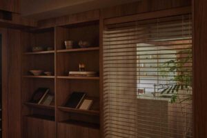 Vestavěná knihovna z tmavého dřeva je propojena s oknem se žaluziemi a umožňuje průhled směrem do zelené části bytu.