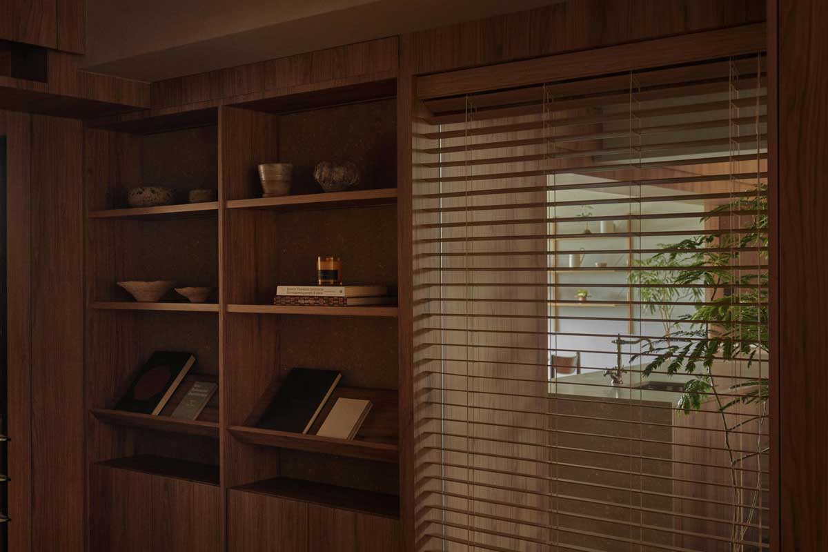 Vestavěná knihovna z tmavého dřeva je propojena s oknem se žaluziemi a umožňuje průhled směrem do zelené části bytu.