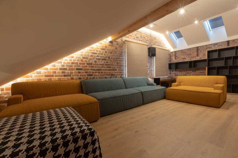 Odpočinková místnost v podkroví s cihlovou stěnou, střešními okny a pohodlnými pohovkami vytváří útulnou relaxační atmosféru.