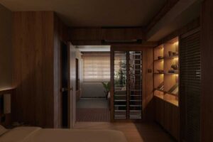 Pohled z ložnice přes dřevěné rámy a lamely odhaluje cihlové prvky a zeleň v centrální obytné části bytu.