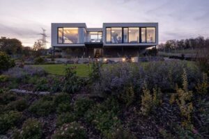 Pohled na moderní vilu ze zahrady s upraveným trávníkem a trvalkovými záhony.