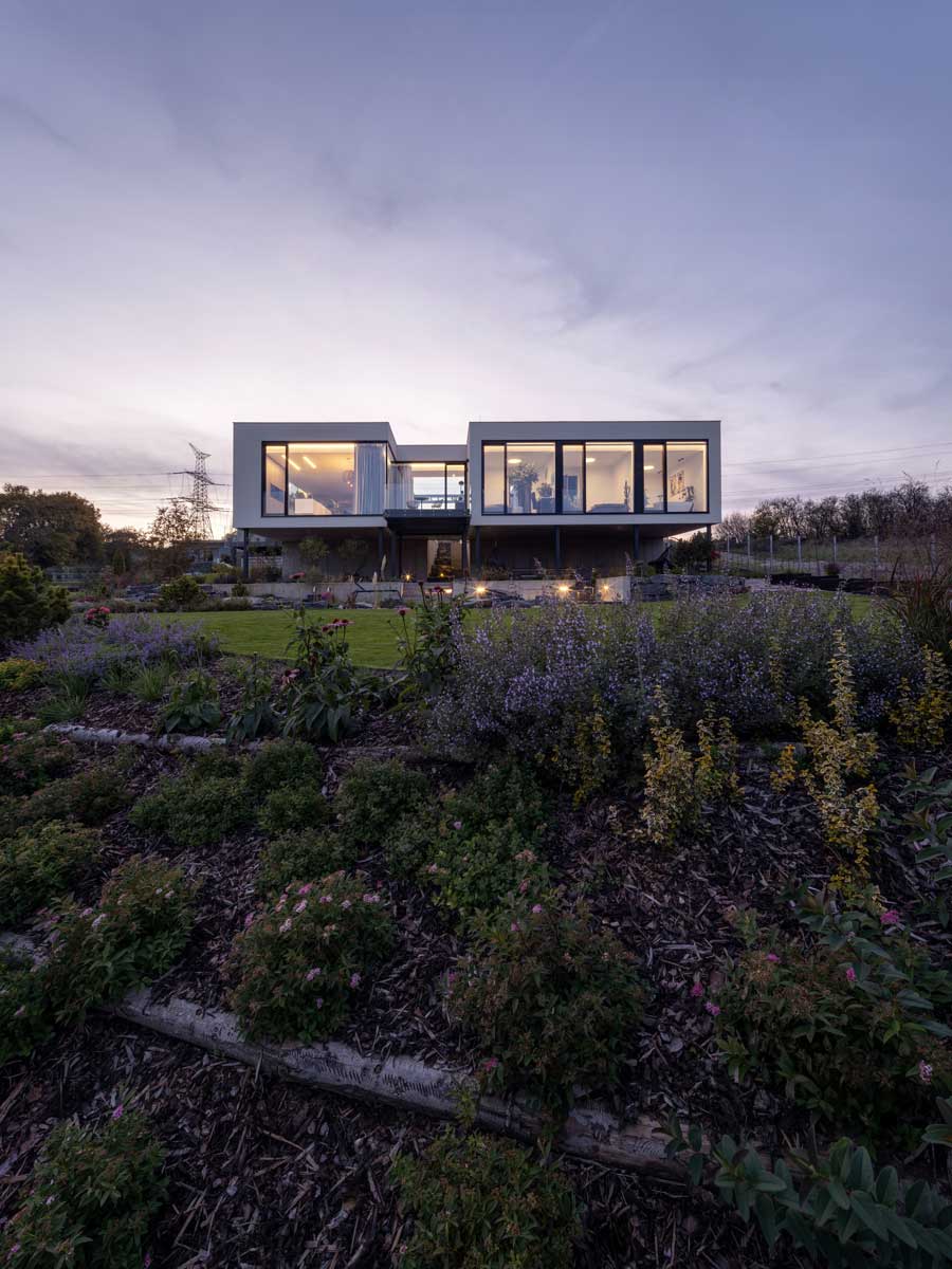 Pohled na moderní vilu ze zahrady s upraveným trávníkem a trvalkovými záhony.