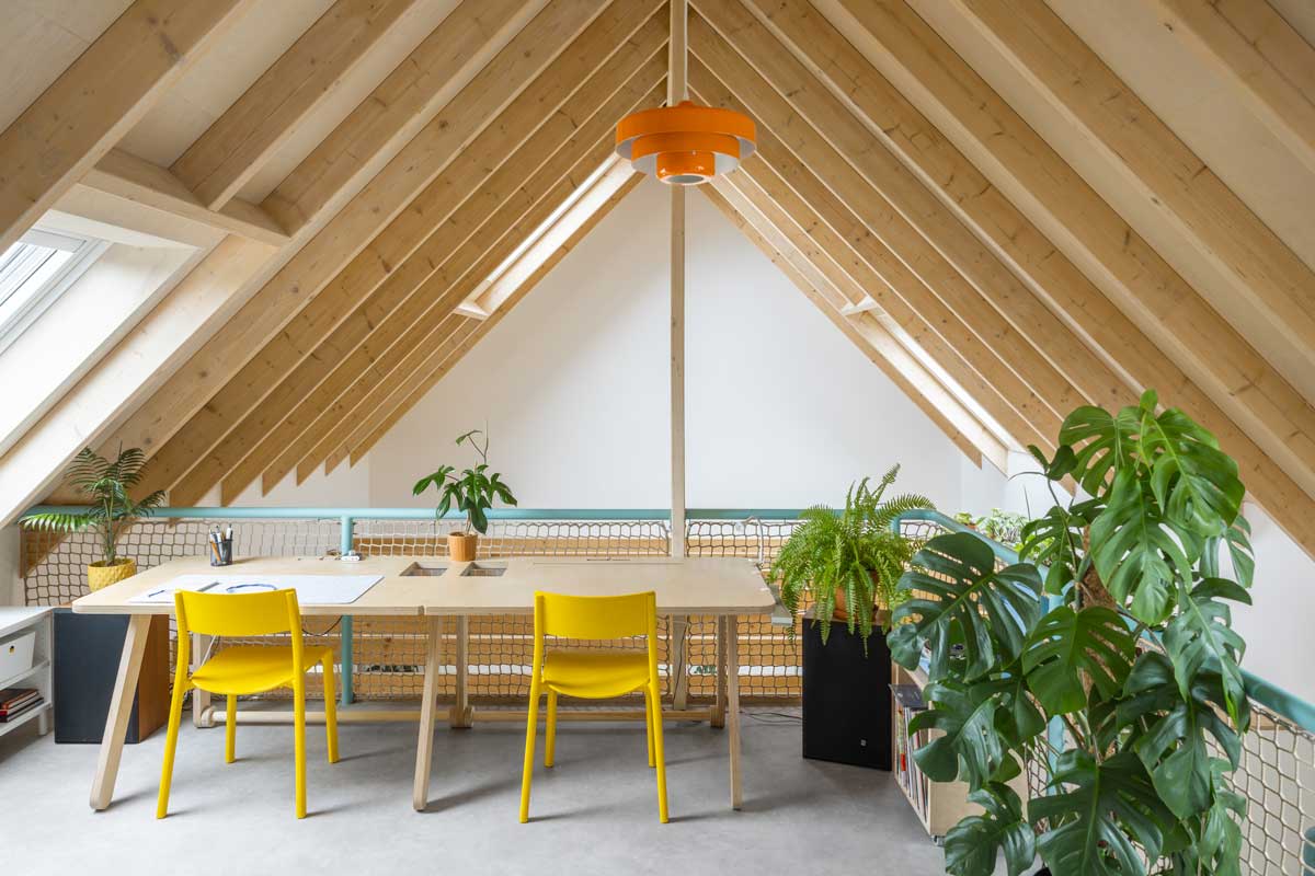 Pracovní stůl pod šikminou se střešními okny v udržitelné dřevostavbě s důrazem na denní osvětlení