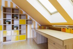 Vestavěná pracovna pod šikminou využívá střešní okno, světlé barvy a modulární úložné prvky pro maximálně funkční pracovní zónu.
