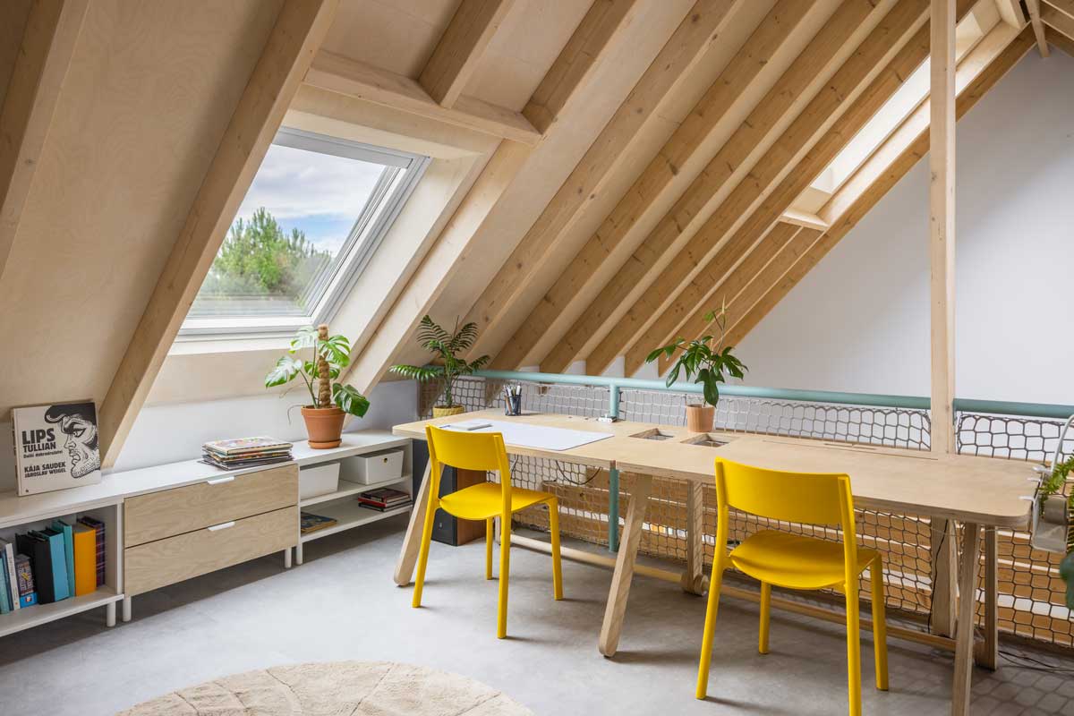 Pracovní kout pod šikminou v udržitelné dřevostavbě s otevřeným krovem a přirozeným denním osvětlením