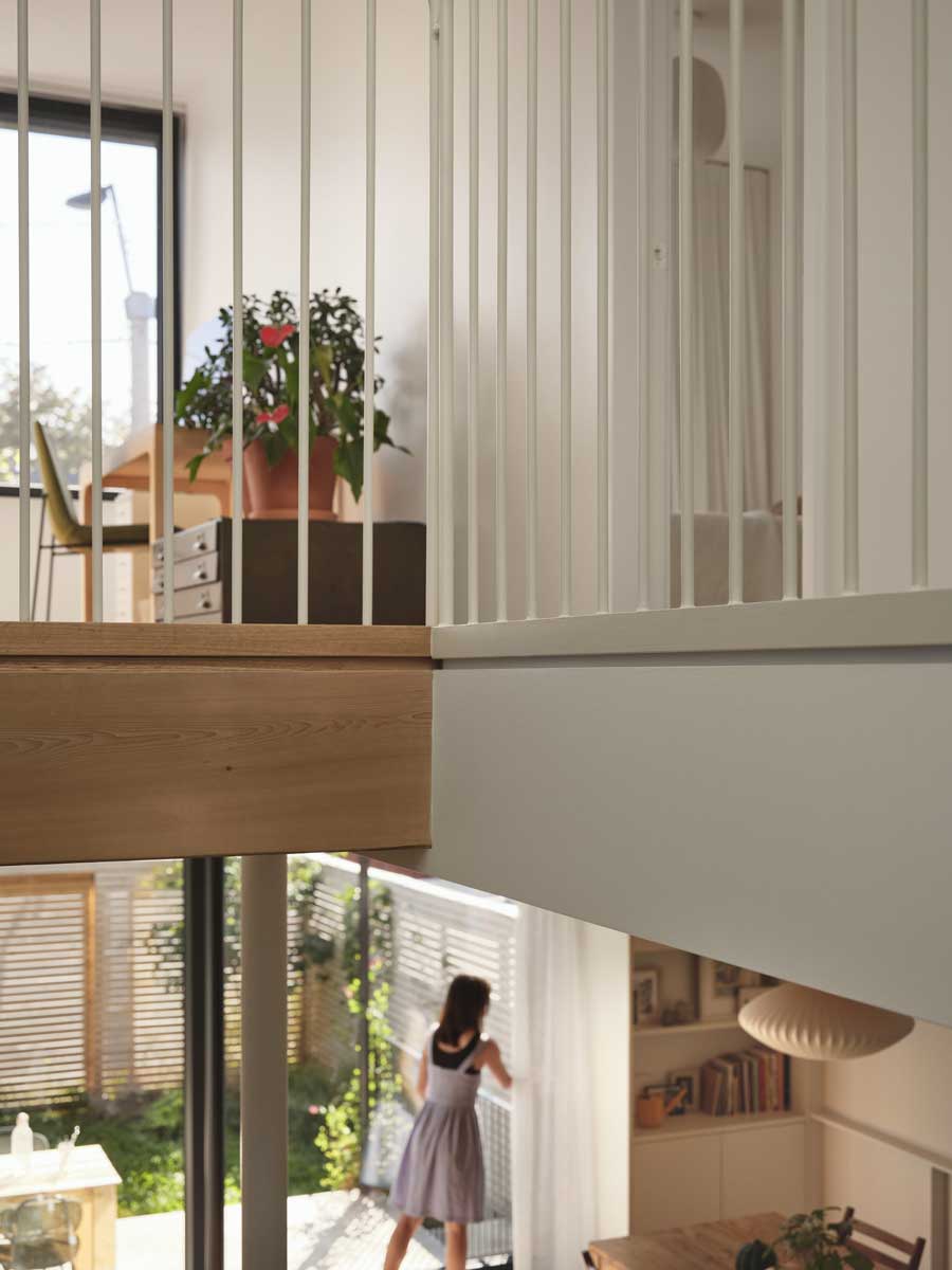 Horní galerie s pracovním koutem, bílým zábradlím a výhledem do obytné části domu.