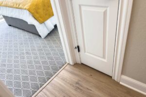 Detail přechodu mezi dvěma podlahovými krytinami u dveří, který zakrývá dilatační spáru a vyrovnává rozdílné výšky podlah.