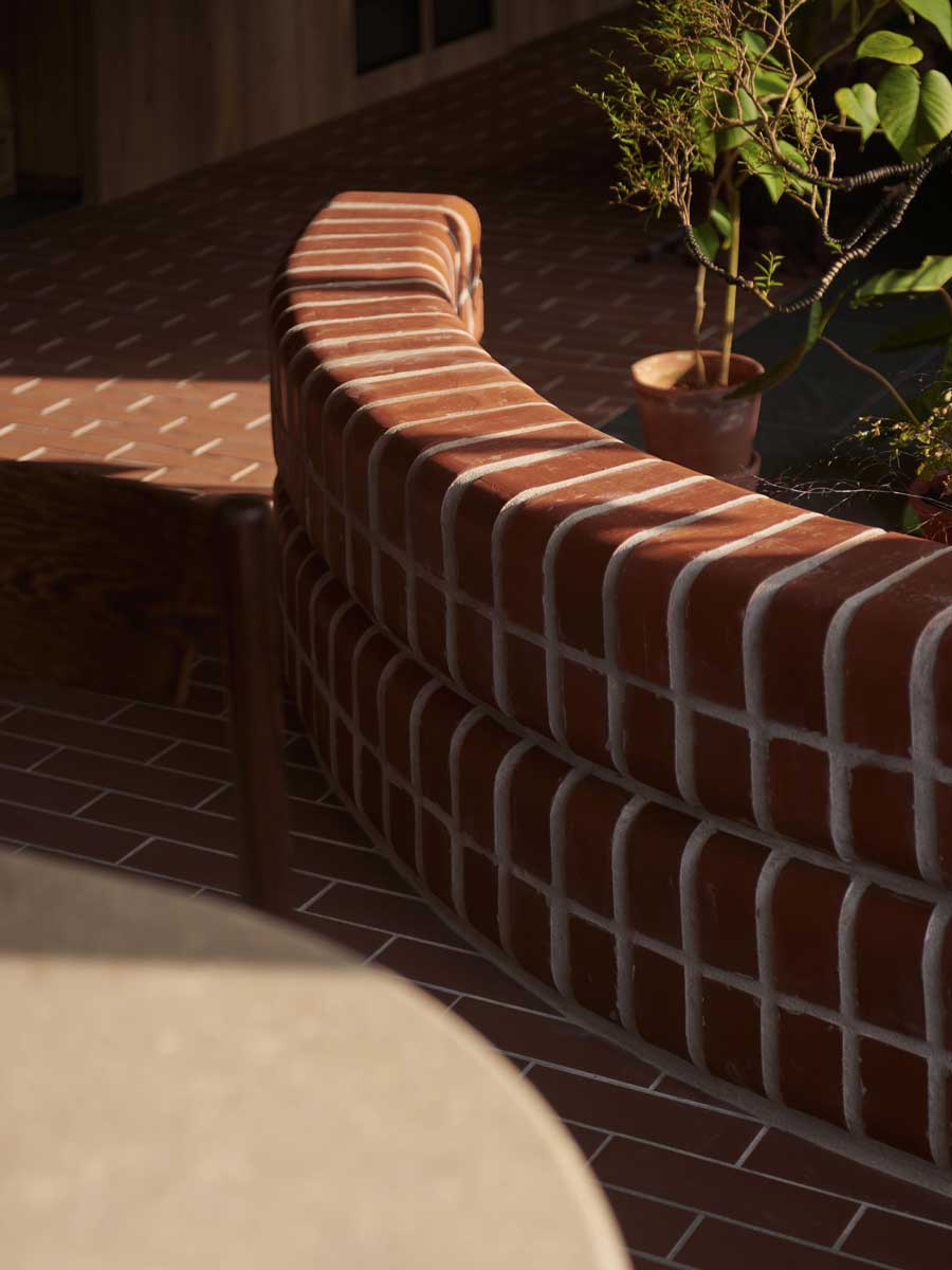 Zakřivená cihlová zídka odděluje jednotlivé části bytu a zároveň slouží jako vizuální i funkční prvek interiéru.