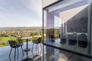 Prosklená terasa s posezením a výhledem na město a okolní kopce.