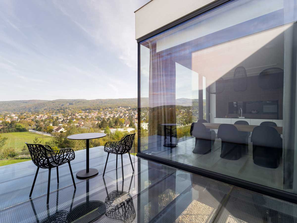 Prosklená terasa s posezením a výhledem na město a okolní kopce.