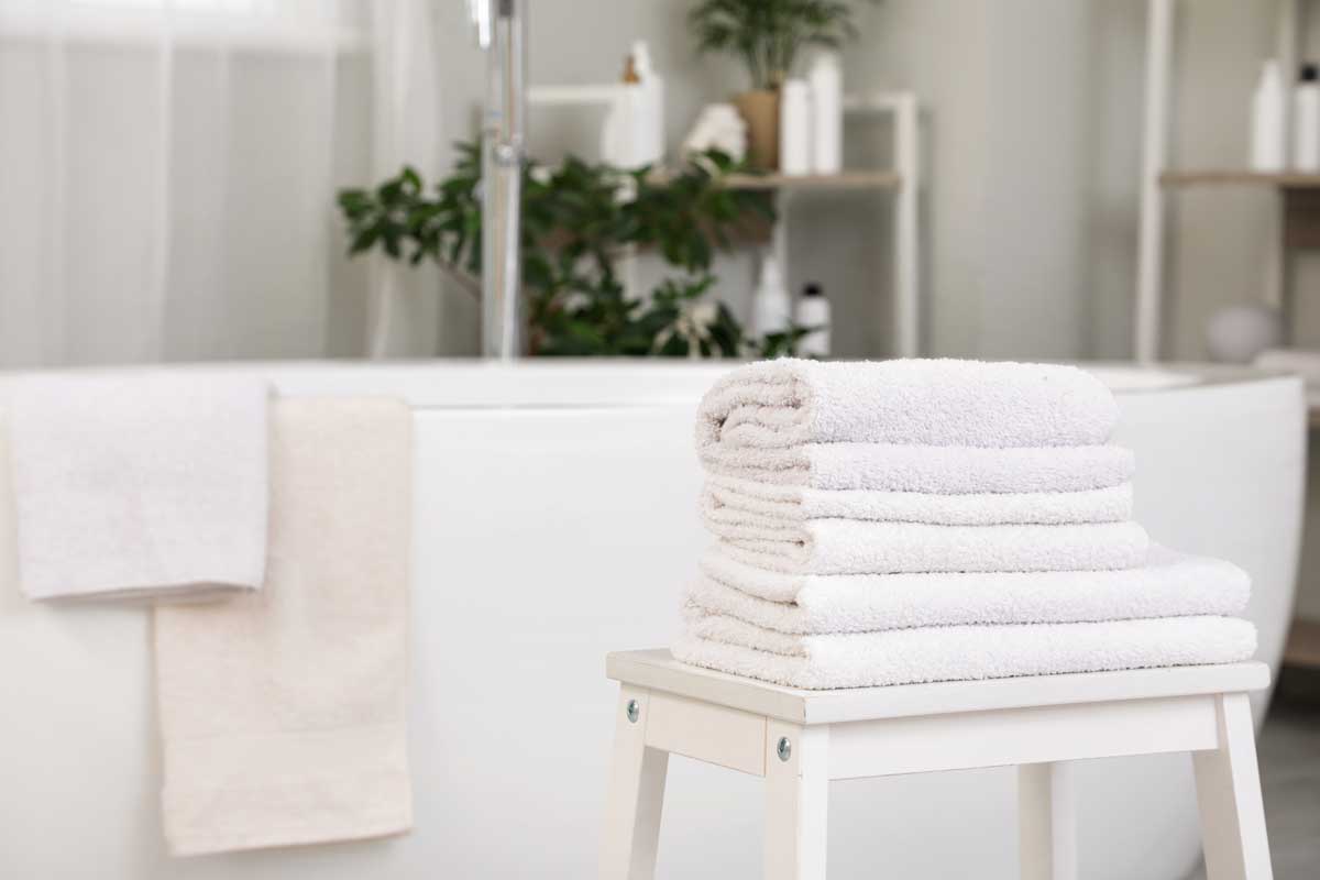 Komínek bílých ručníků položený na stoličce v moderní koupelně s vanou v pozadí.
