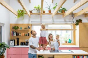 Rodina v otevřené kuchyni nízkoenergetické dřevostavby s ostrůvkem a přiznanými dřevěnými trámy
