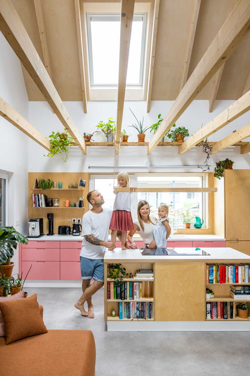 Rodina v otevřené kuchyni nízkoenergetické dřevostavby s ostrůvkem a přiznanými dřevěnými trámy