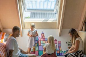 Rodina s dětmi v podkrovním pokoji dřevostavby osvětleném střešním oknem