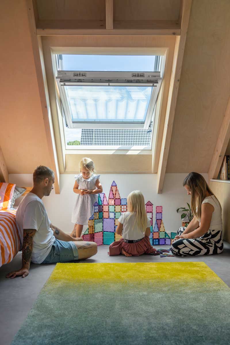 Rodina s dětmi v podkrovním pokoji dřevostavby osvětleném střešním oknem