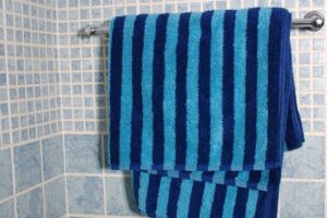 Modře pruhovaný ručník zavěšený na držáku v koupelně s keramickým obkladem.
