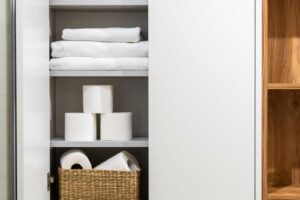 Složené bílé ručníky uložené v uzavřené koupelnové skříňce s košíky na policích.