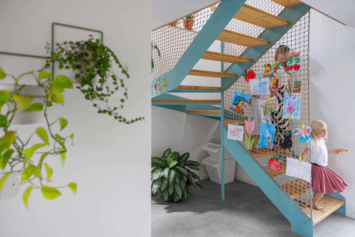 Otevřené schodiště s kovovou konstrukcí a sítí v nízkoenergetické dřevostavbě s prosvětleným interiérem