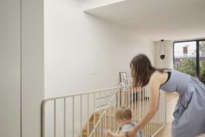 Detail dřevěného schodiště s bílým kovovým zábradlím v minimalistickém interiéru.