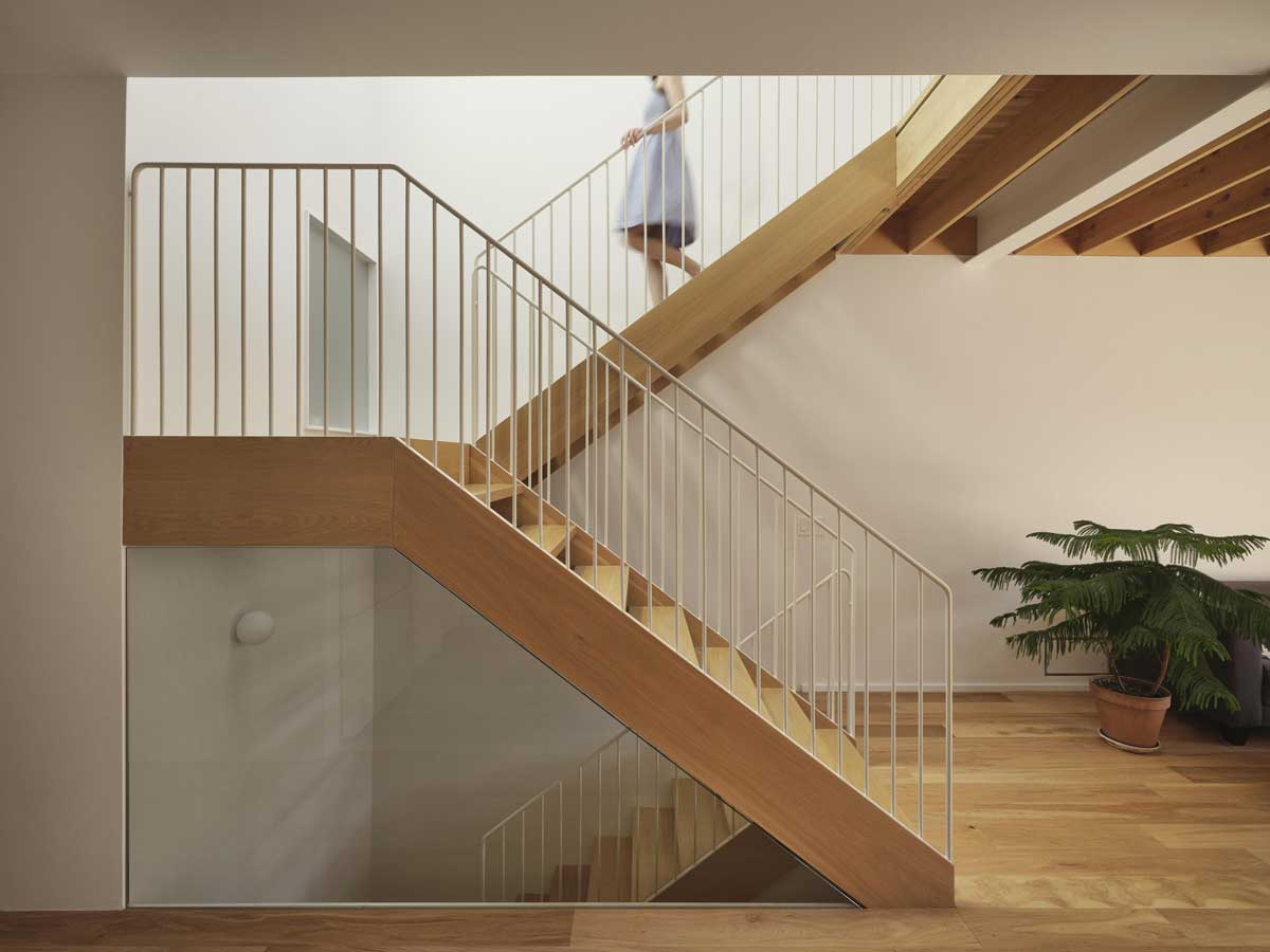 Boční pohled na otevřené dřevěné schodiště procházející dvoupodlažním prostorem.