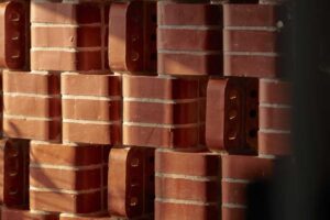 Detail plastické cihlové stěny v kombinaci s čalouněnou sedačkou zdůrazňuje strukturu materiálu a hru světla.