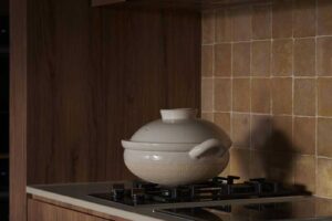 Kuchyňský sporák s keramickým hrncem je zasazen do dřevěné linky s obkladem z malých čtvercových dlaždic v teplém odstínu.