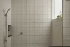 Minimalistický sprchový kout s bílými obklady, nikou na kosmetiku a velkým oknem pro přirozené světlo.