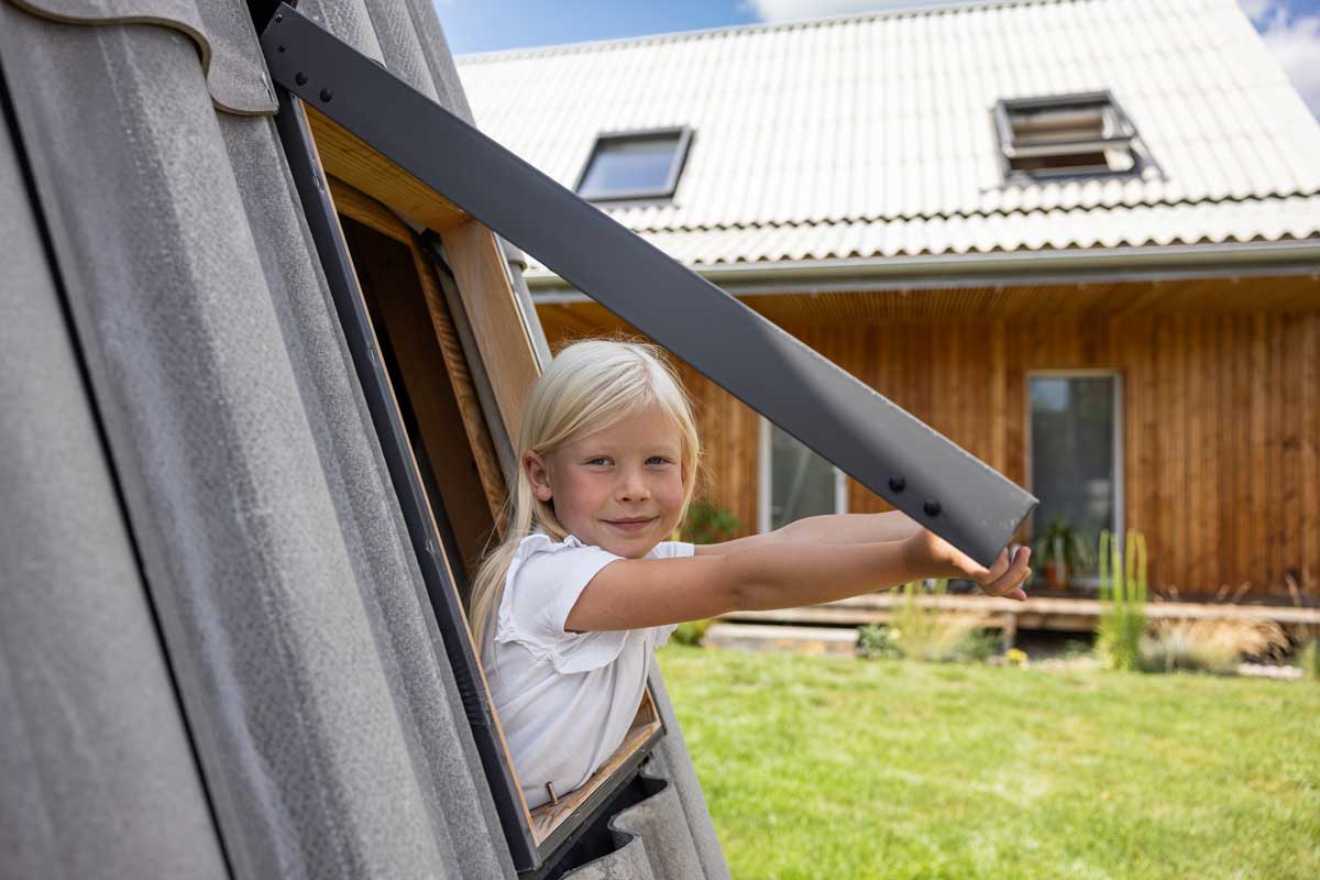 Dítě vyklánějící se ze střešního okna v nízkoenergetické dřevostavbě se sedlovou střechou