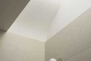 Koupelna s horním světlíkem, světlými stěnami a jednoduchým nástěnným svítidlem.