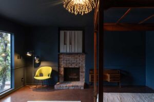 Tmavá ložnice s krbem, výrazným křeslem a tlumeným světlem vytváří intimní prostor určený ke klidu i soustředění.