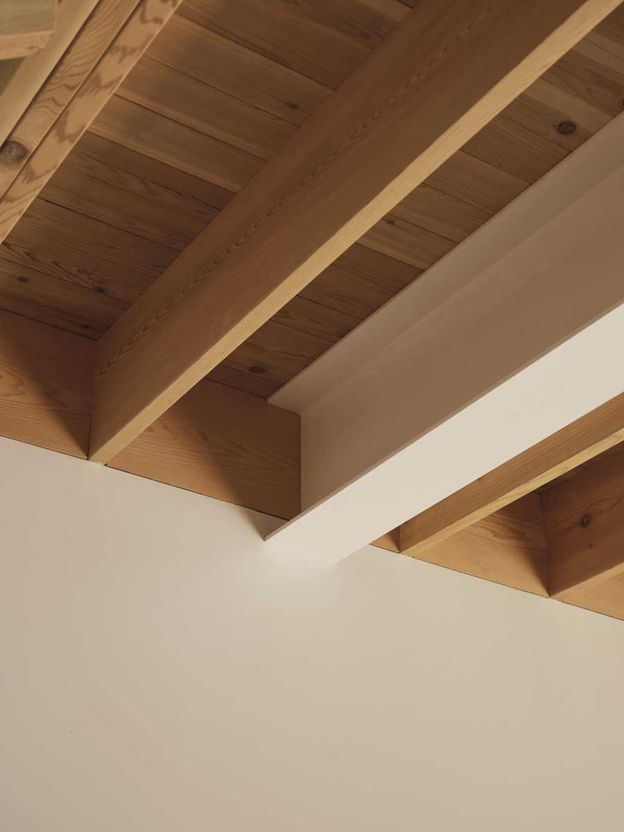 Detail přiznaných dřevěných stropních trámů v kombinaci s bílým stropem.