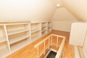 Vestavěné police a nízké úložné systémy podél šikmých stěn efektivně využívají každý centimetr podkrovního prostoru.