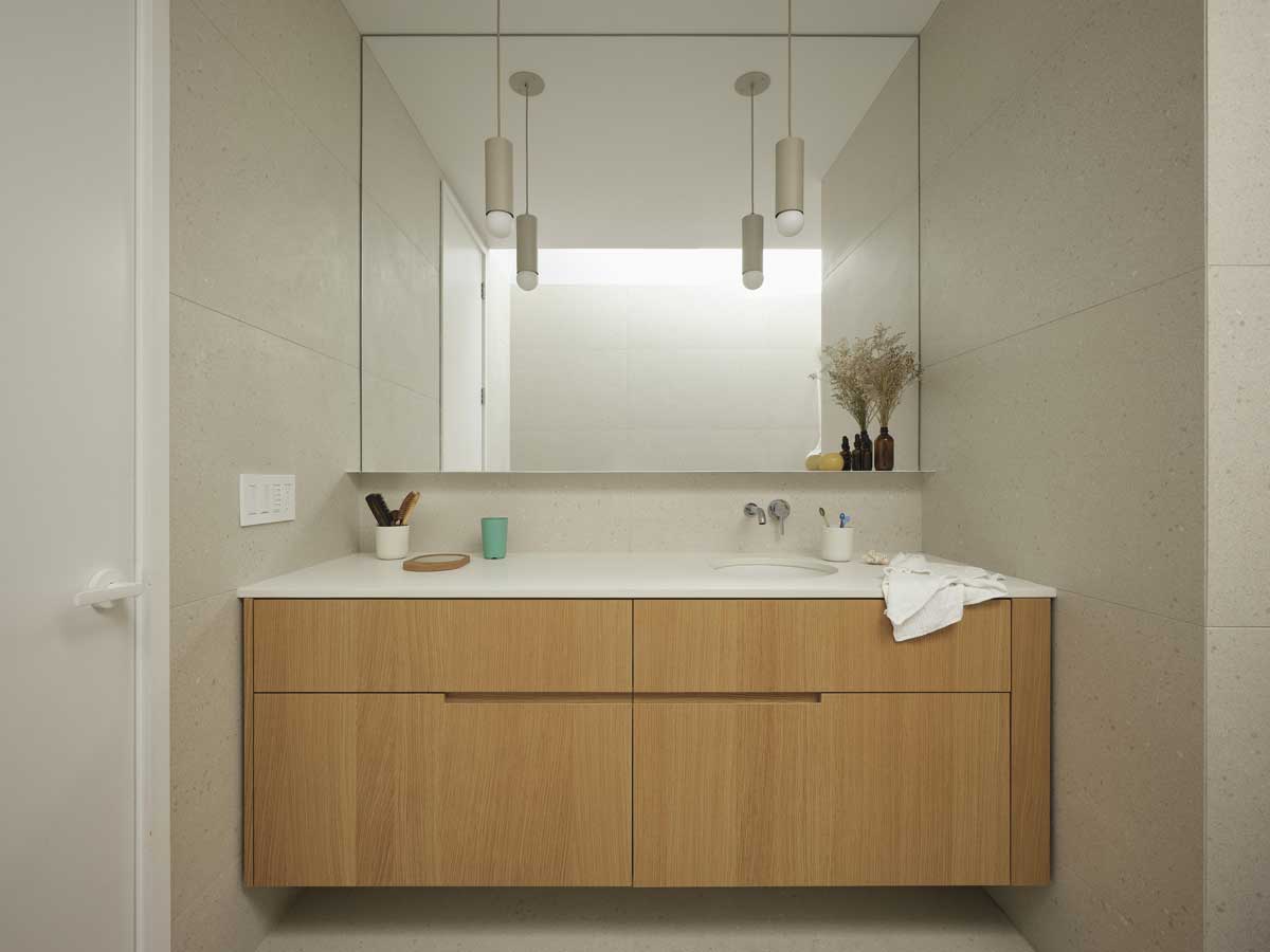 Koupelnová skříňka z masivního dřeva se zapuštěným umyvadlem a velkým zrcadlem přes celou stěnu.