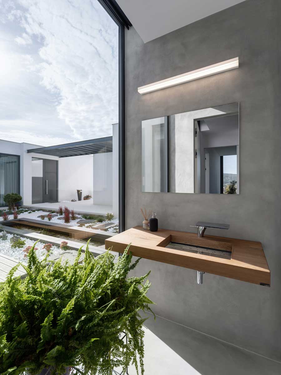 Minimalistická koupelna s betonovou stěrkou a dřevěným závěsným umyvadlem u velkého okna.