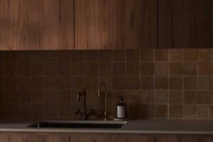 Dřevěná kuchyňská linka s mosaznou baterií a keramickým obkladem vytváří harmonický celek v zemitých tónech.