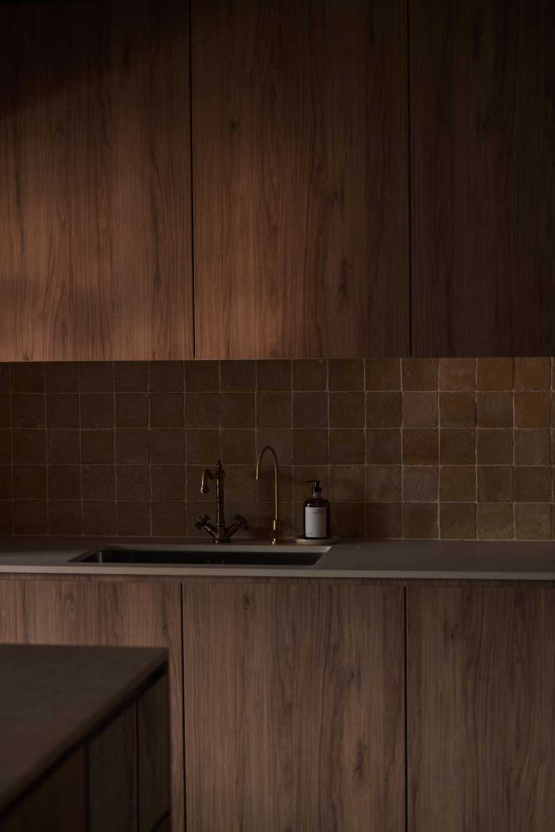 Dřevěná kuchyňská linka s mosaznou baterií a keramickým obkladem vytváří harmonický celek v zemitých tónech.