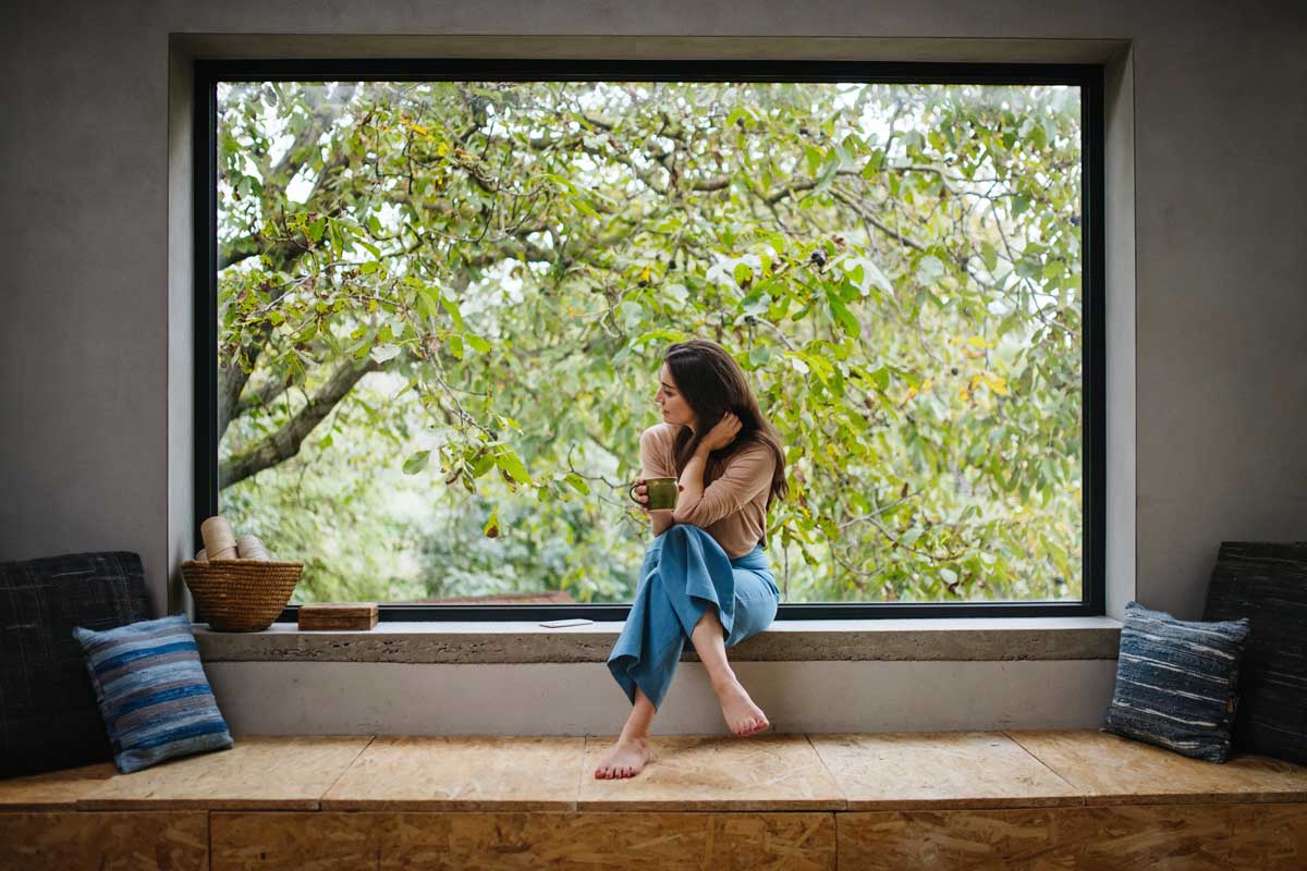 Široké horizontální okno s hlubokým parapetem vytváří klidné místo k sezení a propojuje každodennost s proměnami přírody.