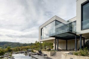 Moderní vila s koupacím jezírkem, betonovou terasou a proskleným balkonem.