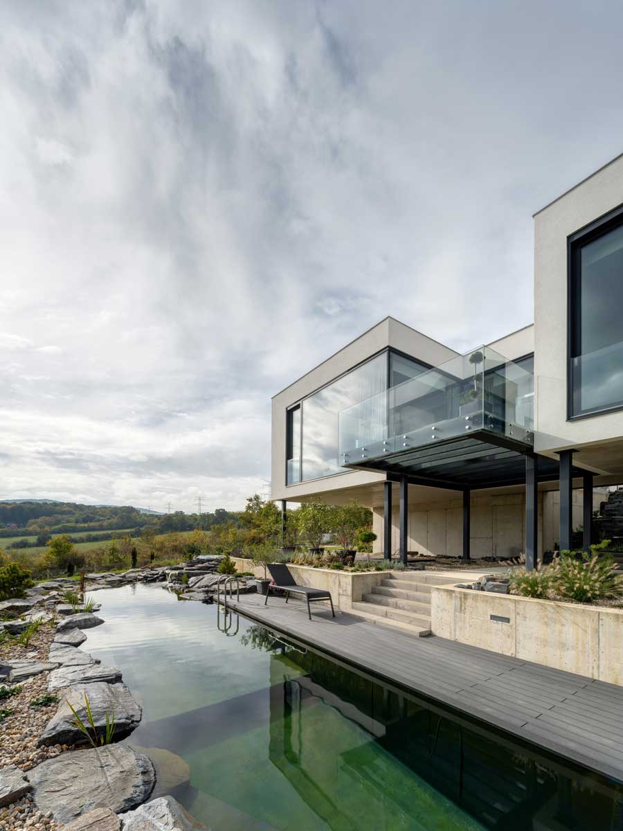 Moderní vila s koupacím jezírkem, betonovou terasou a proskleným balkonem.