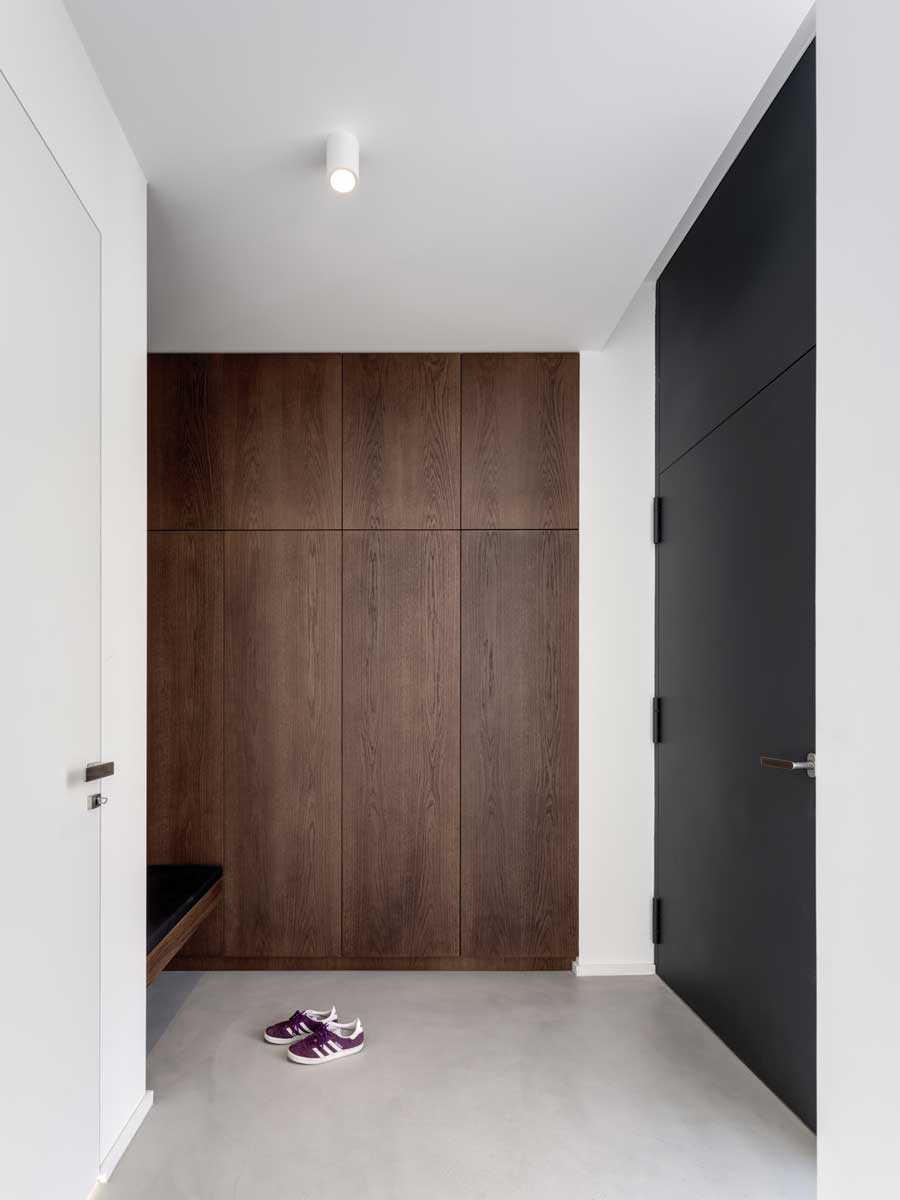 Minimalistická vstupní hala s vestavěnou dřevěnou skříní a tmavými interiérovými dveřmi.