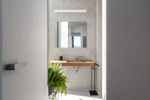 Pohled z chodby do koupelny s betonovou stěrkou a dřevěným umyvadlovým pultem.