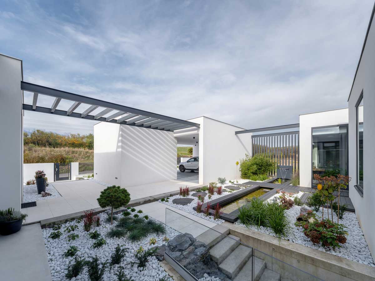 Vstupní zahrada s pergolou, vodním prvkem a výsadbou v bílém kačírku.