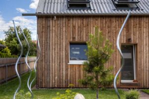 Vyvýšené záhony u udržitelné dřevostavby s fasádou ze sibiřského modřínu a sedlovou střechou